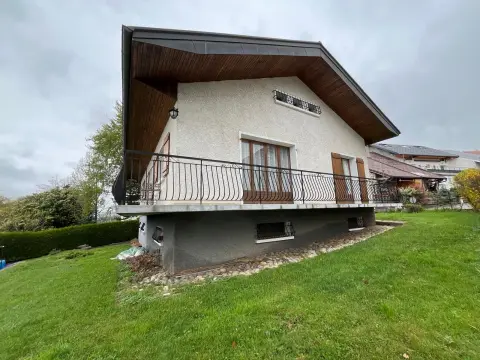 La maison vue du jardin, avec son grand balcon sur toute la longueur de la façade et la pelouse en pente devant.