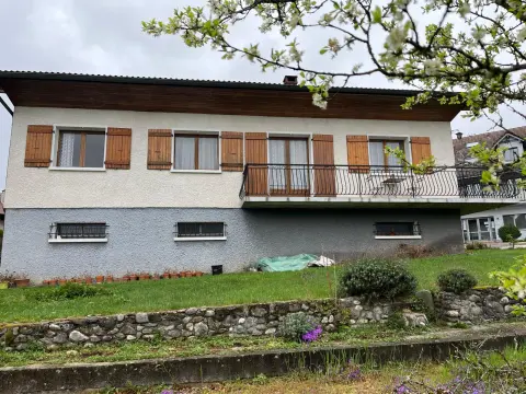 La façade côté jardin sous un pommier en fleurs, avec le balcon et le mur de pierres sèches en contrebas.