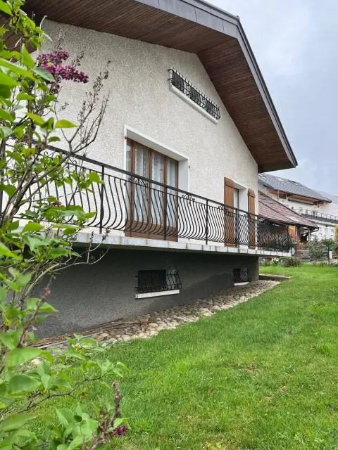 Le balcon vu depuis la pelouse, soutenu par le soubassement de la maison, avec la table et les chaises installées dessus.