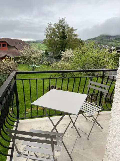 La table et les chaises pliantes installées sur le balcon, ouvertes sur le jardin et la campagne.
