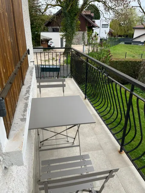 Le balcon et sa rambarde en fer forgé, avec la vue dégagée sur les prés et les toits du village.