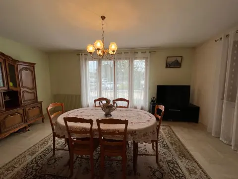 La salle à manger, sa grande table ovale, ses six chaises et son lustre, avec la télévision sur le côté.
