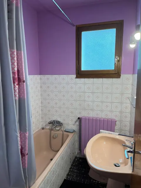 La salle de bains et sa baignoire, avec radiateur et fenêtre donnant sur l'extérieur.